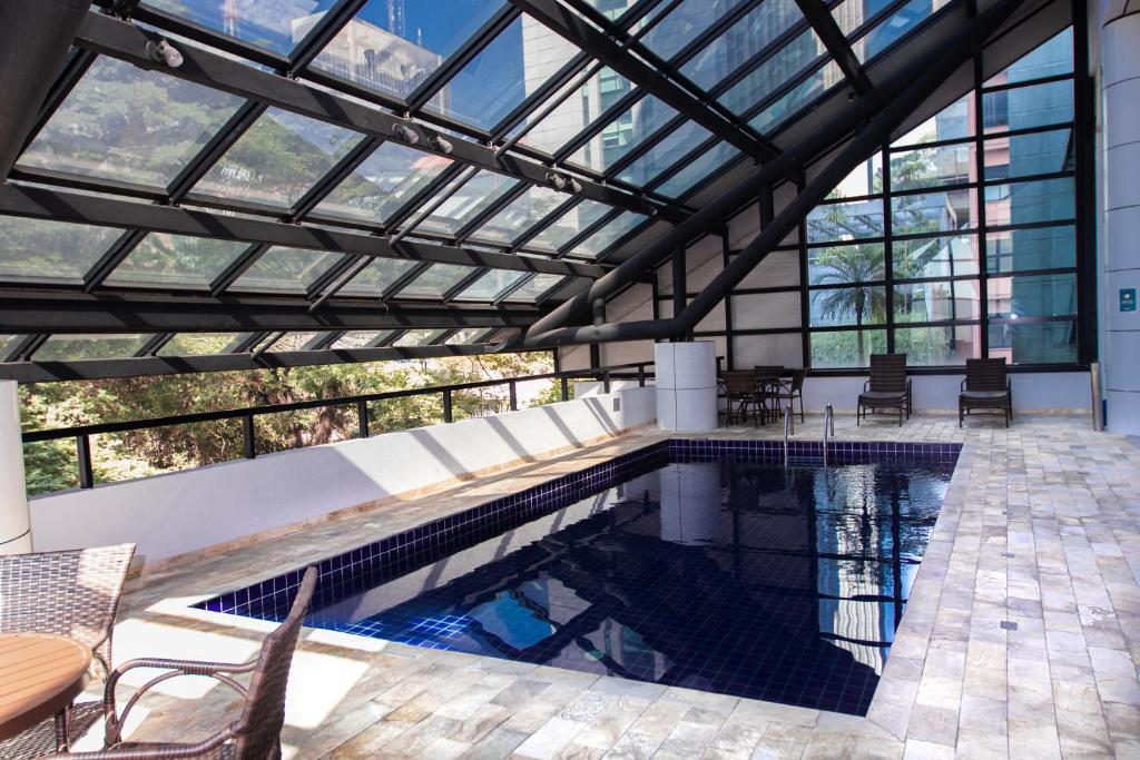 Uma piscina grande coberta, a cobertura é transparente possibilitando ver o céu e os prédios.