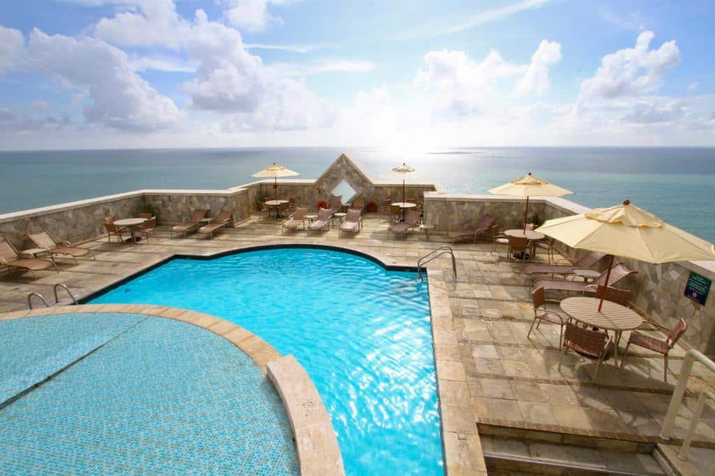 Uma piscina com cadeiras ao redor, a vista para o mar.