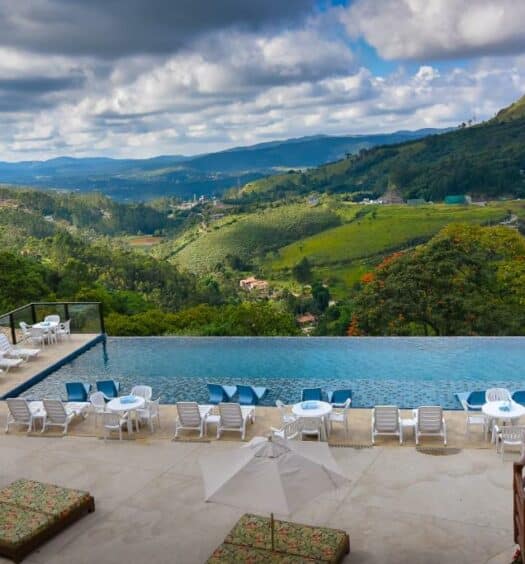 Uma piscina no meio, com borda infinita e vista para a serra. No Hotel Refúgio Vista Serrana. Ao redor cadeiras de tomar sol. Foto para ilustrar post sobre Pousadas na Serra da Cantareira.