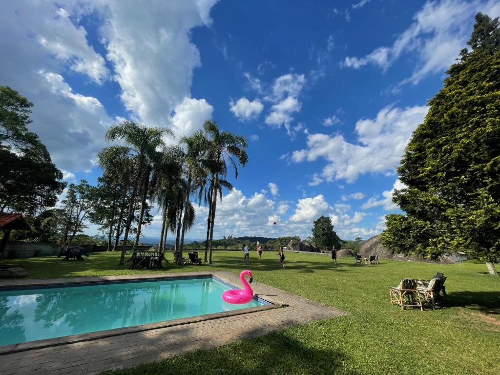 Piscina da Pousada e restaurante Refúgio Dinamarca. Uma piscina grande com uma boia rosa de flamingo. Ao redor um terreno plano e todo com grama. Foto para ilustrar post sobre Pousadas na Serra da Cantareira.