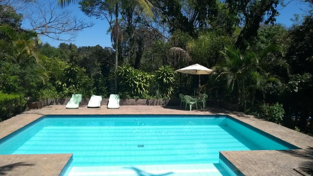 Piscina no Refúgio Pasárgada Guest House. Uma piscina grande, ao redor cadeiras e árvores. Foto para ilustrar post sobre Pousadas na Serra da Cantareira.