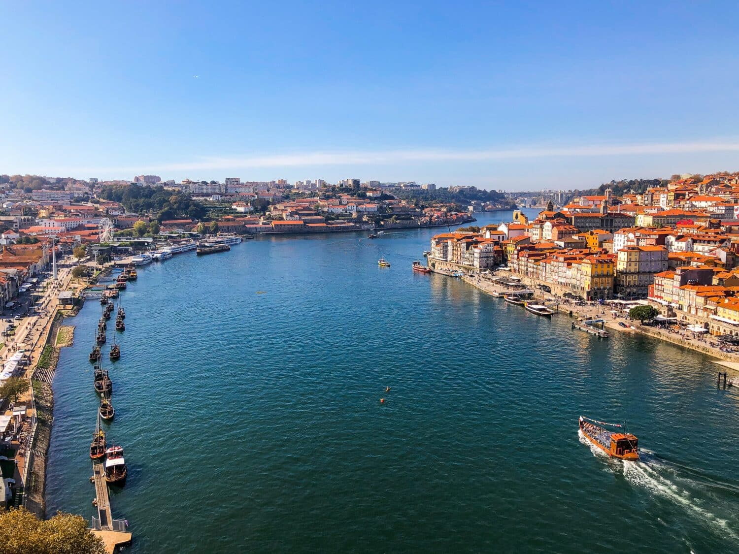 Imagem do cais de Porto em Portugal durante o dia com o rio no meio e em volta casas.