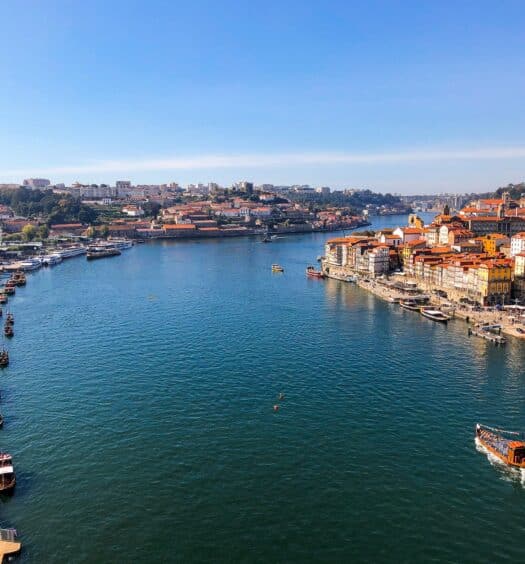 Imagem do cais de Porto em Portugal durante o dia com o rio no meio e em volta casas.