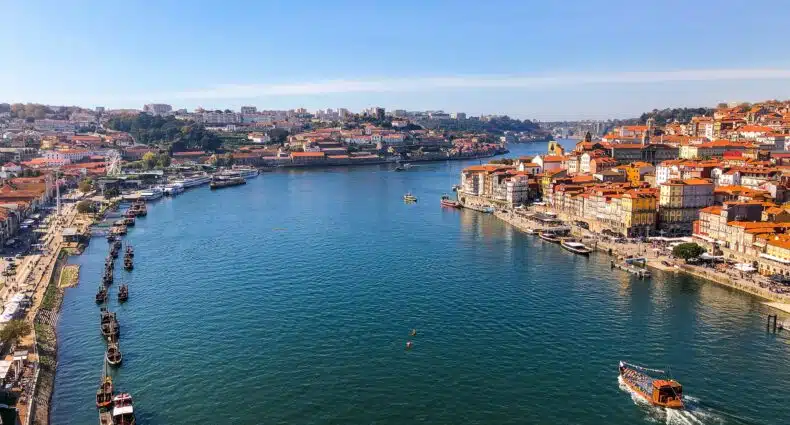 Imagem do cais de Porto em Portugal durante o dia com o rio no meio e em volta casas.