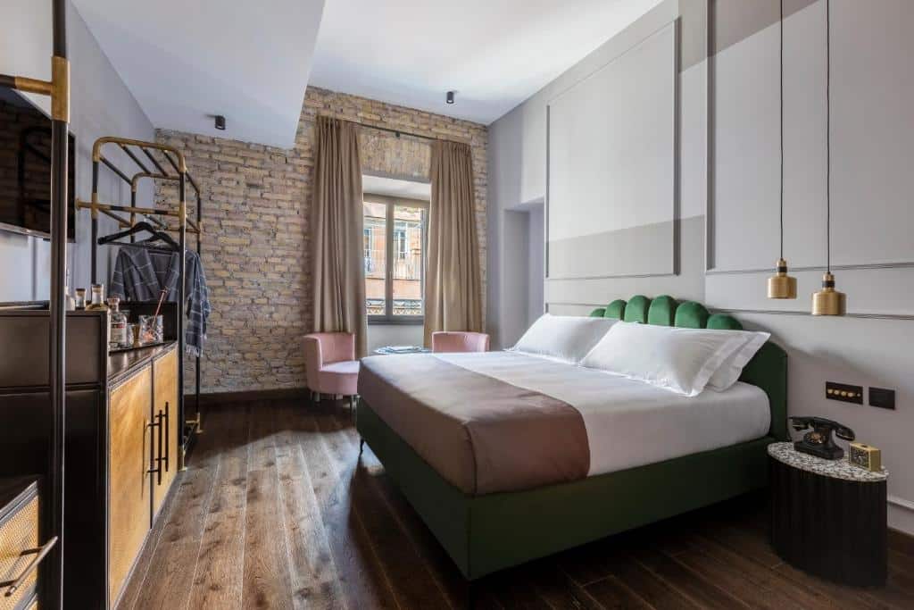 quarto do Chapter Roma, um dos hotéis no centro em Roma, com cama de casal grande, mesinha e luminária, com decoração ao estilo industrial com tons de verde, luminárias compridas e janelas com cortinas claras, há um balcão com tv à frente e uma estante aberta