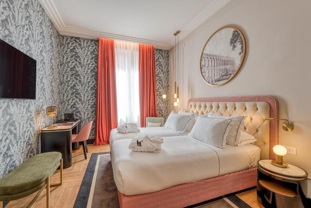 quarto do H10 Palazzo Galla, um dos melhores hotéis no centro de Roma, com cama de casal grande, espelho redondo acima, mesa com poltrona, e tv à rente, com papel de parede monocromático em cinza e todos os detalhes em rosa claro, há, ainda, uma janela comprida com cortinas