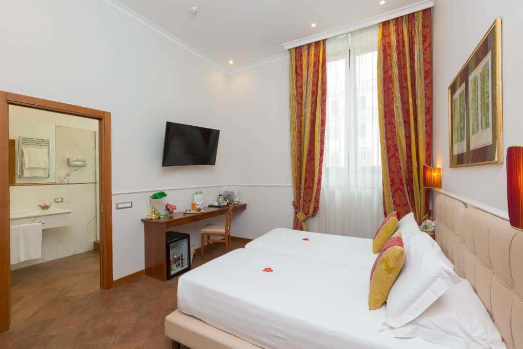 quarto do Hotel Milton Roma, um dos melhores hotéis baratos em Roma, com camas juntadas para formar uma maior, janela grande com cortinas coloridas em tons de amarelo e laranja, à frente, tv e cômoda, e há entrada para o banheiro amplo