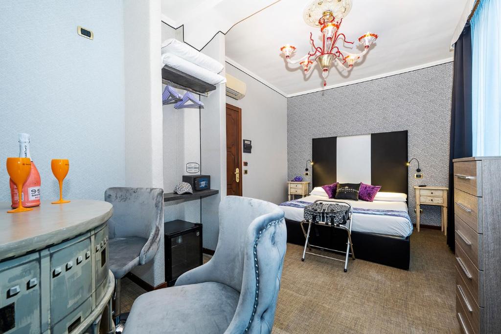 quarto do Hotel Relais Dei Papi, um dos hotéis baratos em Roma, com cama de casal, lustre rebuscado, duas poltronas grandes em tons de azuis claros, um balcão trabalhado  com taças à frente, há também cabides disponíveis e mesas com luminária de ambos os lados da cama