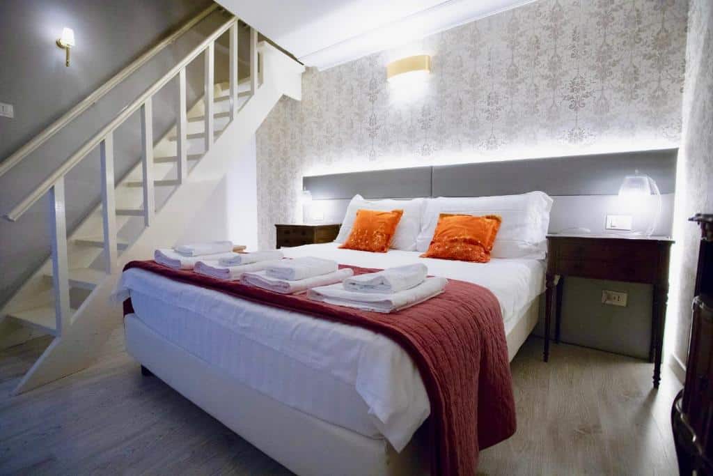 quarto do Navona Residenza de Charme, um dos hotéis no centro de Roma, com cama de casal grande com detalhes em laranja e vermelho, há mesinha e luminária em ambos os lados e uma escada