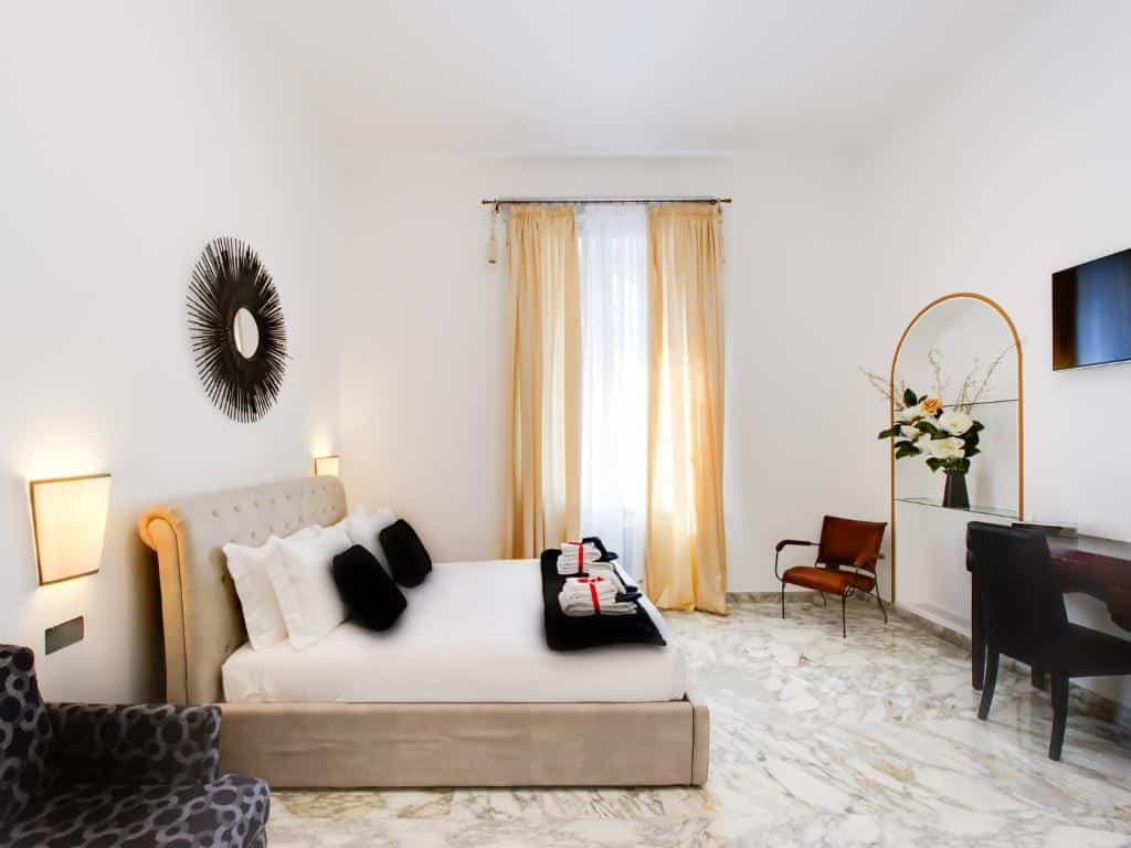 quarto do Queen Palace Suites, um dos hotéis no centro de Roma, com cama de casal com luminárias de ambos os lados, com tv à frente, há poltrona, um quadro em forma de sol e a decoração tem tons de bege e motivos florais, com uma janela comprida do outro lado