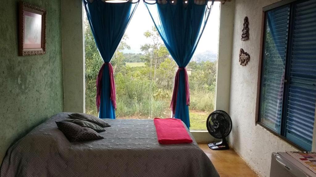 interior do quarto da pousada aldeia da serra lapinha com uma cama de casal à esquerda com uma janela de vidro ampla que dá vista panorâmica para a natureza