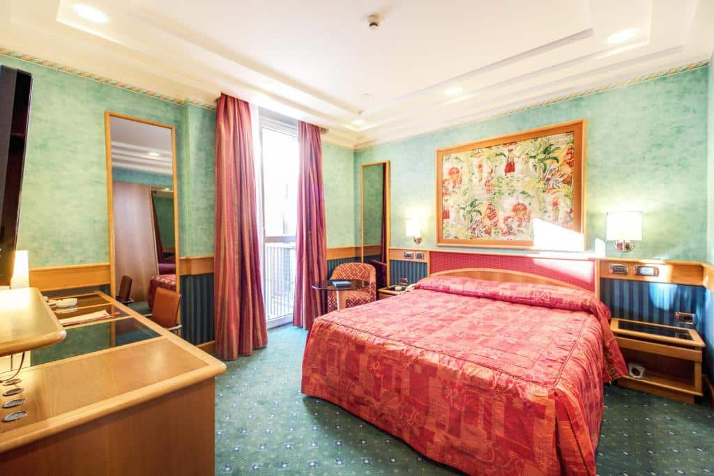 Quarto do Brunelleschi Hotel com uma cama de casal, uma pequena varandas, duas mesinhas de cabeceira, uma mesinha de escritório com uma cadeira giratória, um espelho e uma televisão, para representar hotéis baratos em Milão