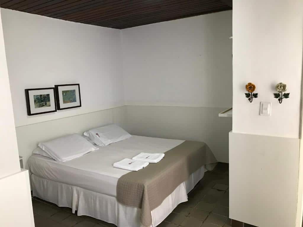 Quarto de hotel simples, com cama de casal, paredes brancas e pequenos quadros decorativos. Imagem para ilustrar o post hotéis em Teresina.