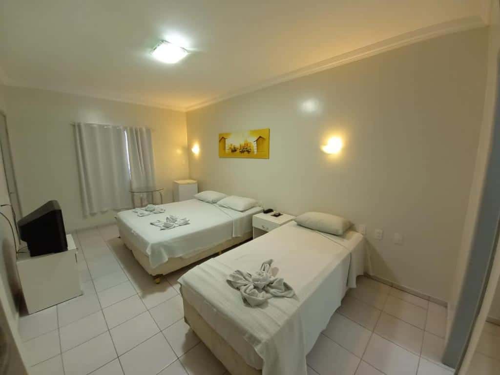 Quarto de hotel com uma cama de casal, uma cama de solteiro, móveis, cortinas e paredes brancas com pequeno quadro decorativo amarelo. Imagem para ilustrar o post hotéis em Parnaíba.