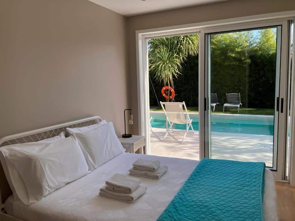 Quarto da Casa dos Pinheiros 109 - Private Villa with pool & heated SPA com cama de casal a frente e do lado esquerdo do quarto uma cômoda com luminária e uma porta de vidro que dá acesso a piscina. Representa hotéis no Porto.