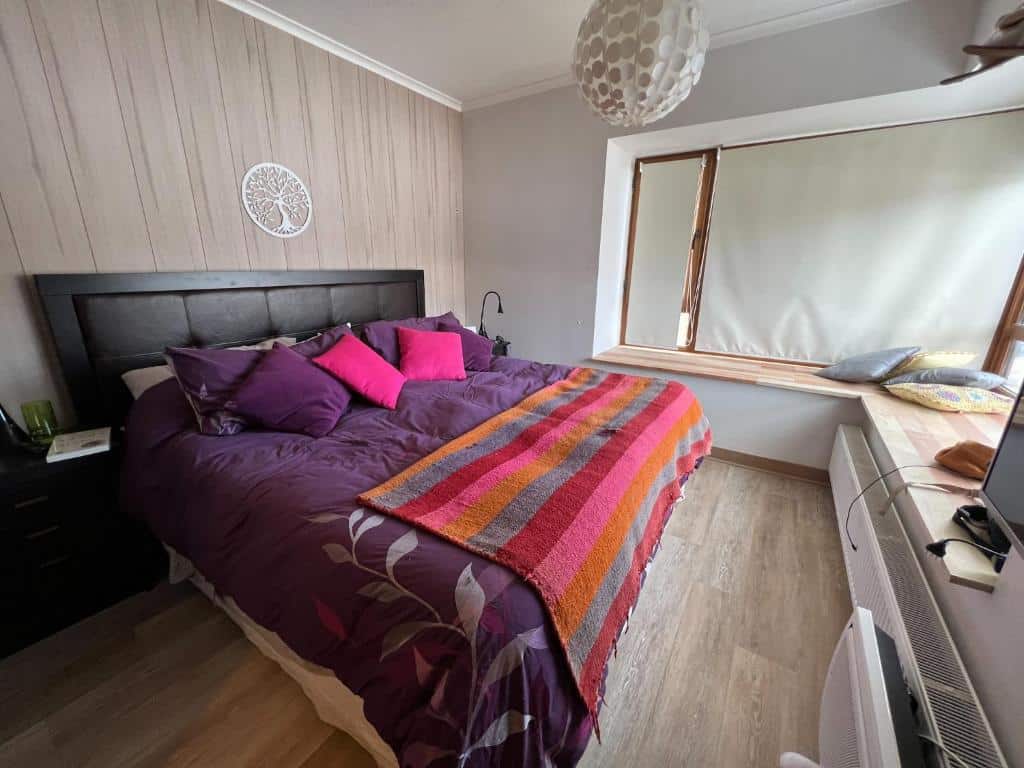 Quarto do Departamento Valle Nevado Ski Resort Chile Ski in – Ski out com cama de casal do lado esquerdo com duas cômodas de madeira ao lado e em frente a cama um balcão com TV.