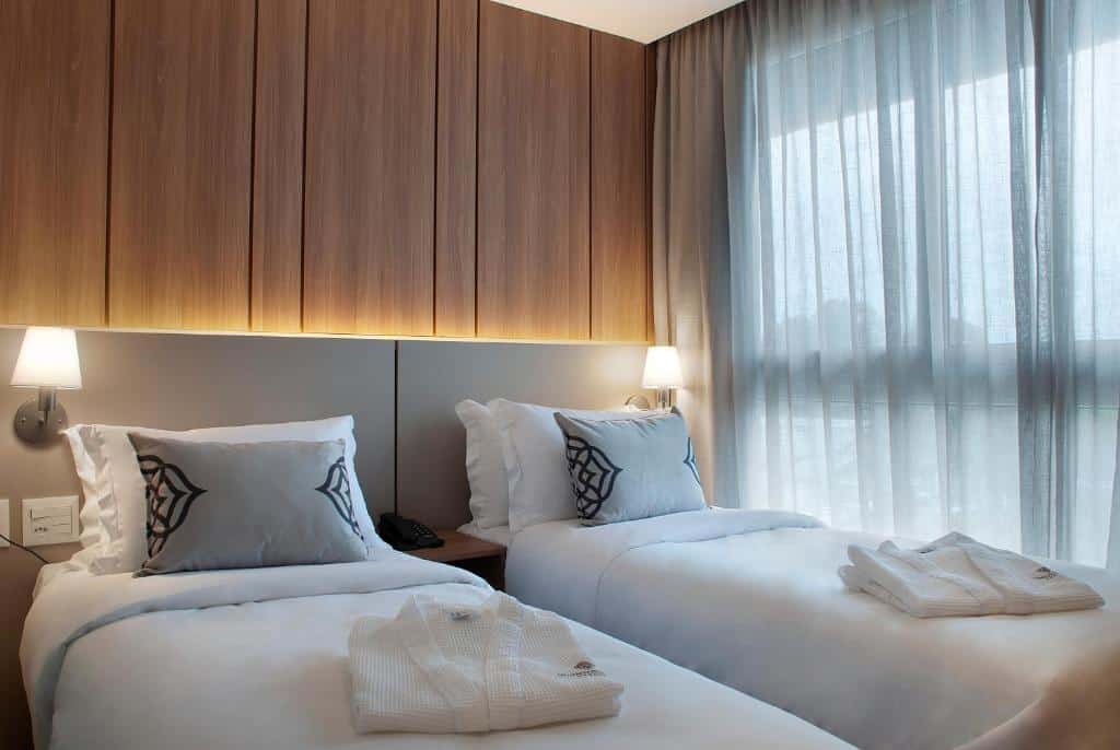 quarto com duas camas de solteiro do Exclusive Gramado Hotel & Spa by Gramado Parks mostrando dois roupões brancos em cima de cada colchão