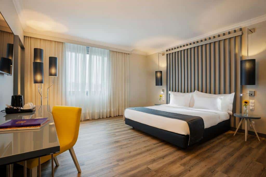 Quarto do HF Ipanema Park com cama de casal do lado direito, com duas cômodas ao lado e em frente a cama uma mesa ampla com cadeira e TV pendurada na parede. Representa hotéis no luxo do Porto.