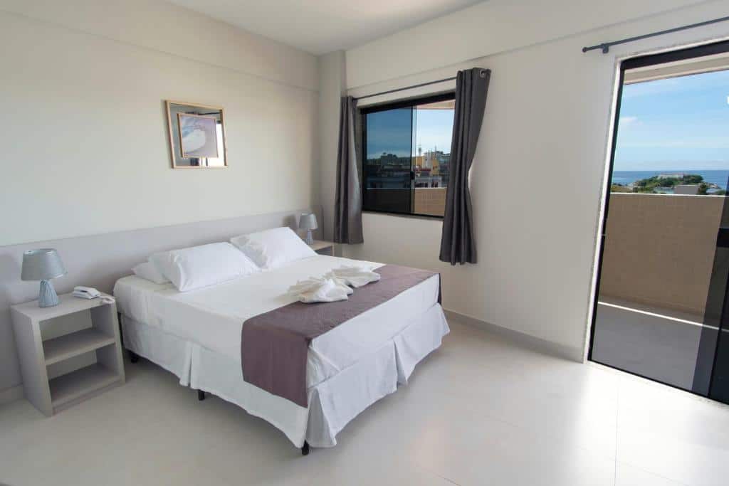 Quarto de hotel simples com paredes brancas, cama de casal e varanda com vista para o mar. Imagem para ilustrar o post hotéis em Cabo Frio.