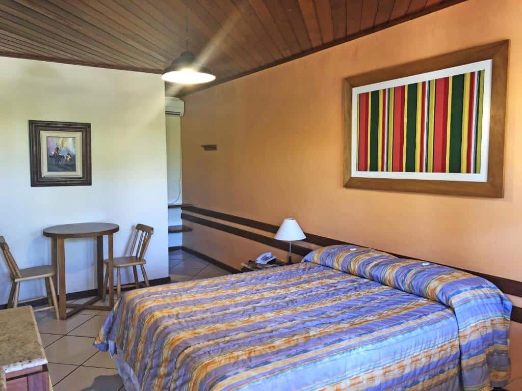 Quarto de hotel com uma parede laranja, outra parede branca, quadros decorativos e cama de casal. Imagem para ilustrar o post hotéis em Cabo Frio.