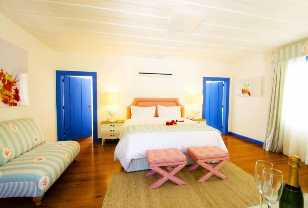 Quarto de hotel espaçoso com grande casa de casal, duas portas azuis, sofá e taças com champagne. Imagem para ilustrar o post hotéis em Cabo Frio.
