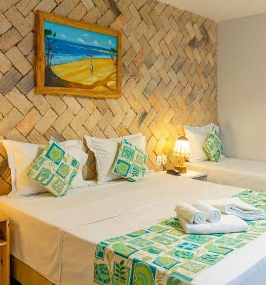 Quarto de hotel com uma cama de casal, uma cama de solteiro, decoração em tons de marrom, branco e verde, luminárias amarelas e um quadro decorativo. Imagem para ilustrar o post hotéis em Parnaíba.