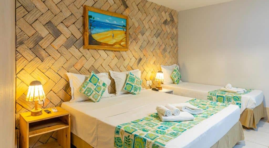 Quarto de hotel com uma cama de casal, uma cama de solteiro, decoração em tons de marrom, branco e verde, luminárias amarelas e um quadro decorativo. Imagem para ilustrar o post hotéis em Parnaíba.