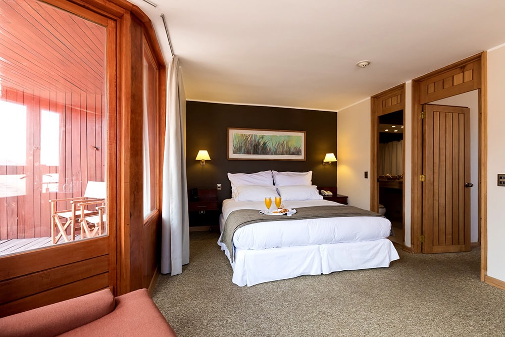Quarto do Hotel Valle Nevado com cama de casal no centro do quarto com duas cômodas ao lado. Representa onde ficar no Valle Nevado.