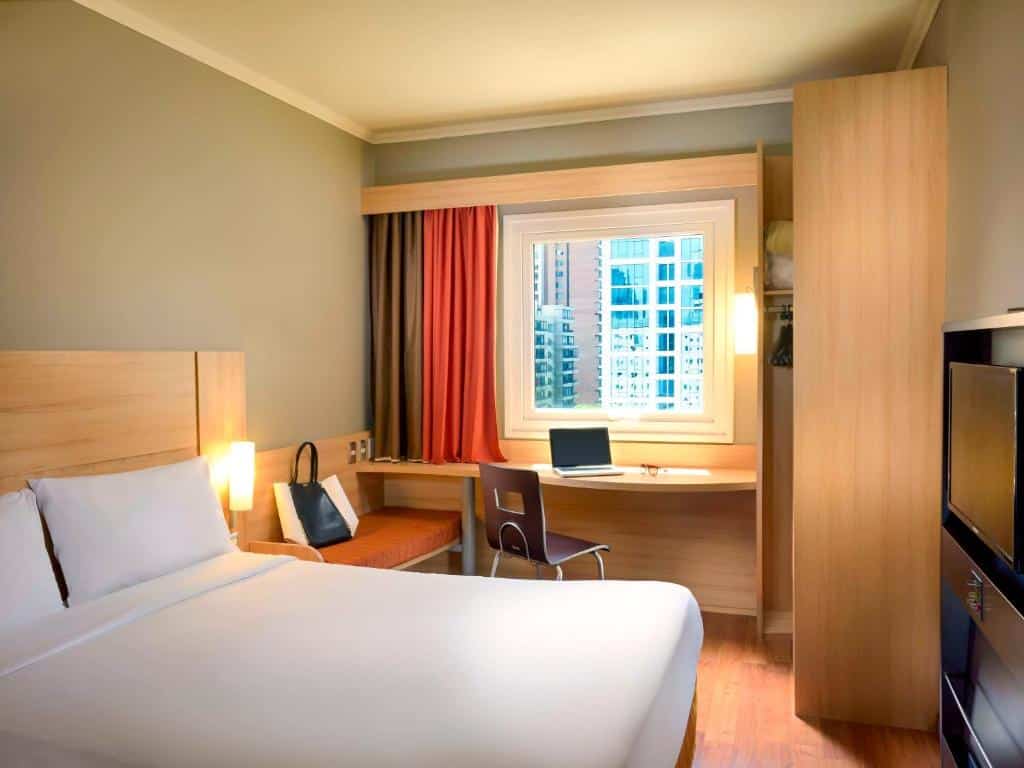 Quarto do ibis Santiago Las Condes Manquehue com cama de casal do lado esquerdo e do lado esquerdo do quarto mesa de trabalho com janela. Representa hotéis Mercure em Santiago.