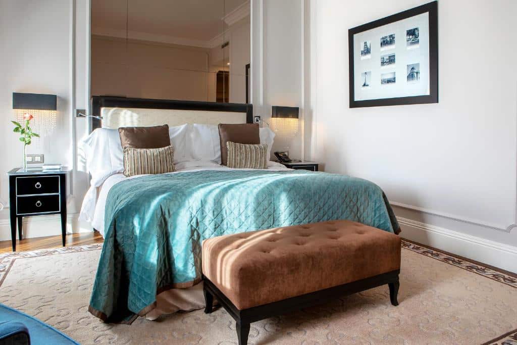 Quarto do InterContinental Porto – Palacio das Cardosas, an IHG Hotel com cama de casal do lado esquerdo, duas cômodas ao lado da cama e no pé da cama um banco estofado. Representa hotéis de luxo no Porto.
