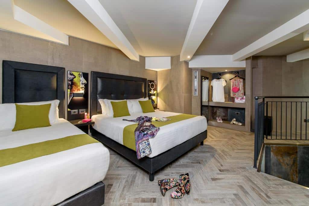 Quarto do Just Hotel Milano com uma cama de casal e uma de solteiro, um armário em conceito aberto, as cabeceiras são em courino e contam com luminárias