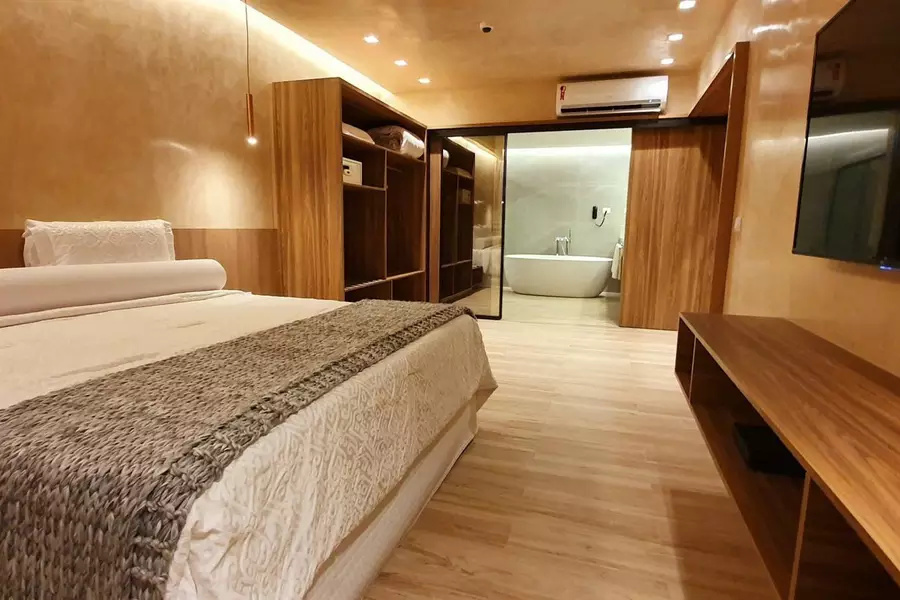Quarto de hotel de luxo com grande cama de casal, móveis em madeira, ar-condicionado e banheira ao fundo. Imagem para ilustrar o post hotéis em Teresina.
