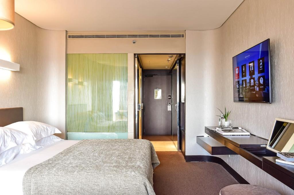 Quarto do Porto Palácio Hotel by The Editory com cama de casal do lado esquerdo e uma mesa a frente da cama com uma TV. Representa hotéis de luxo no Porto.
