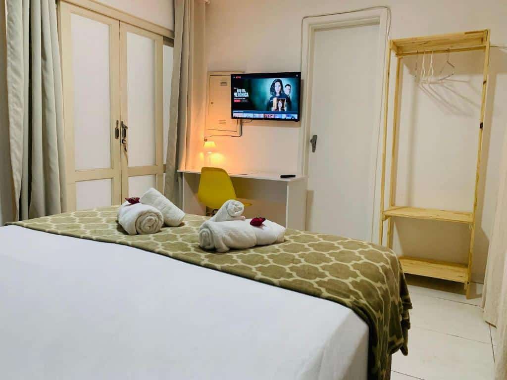 Uma cama de casal, na frente uma televisão e uma mesa de escritório. Ao lado um espaço para pendurar a roupa. Foto para ilustrar post sobre hotéis perto do Hospital Albert Einstein.