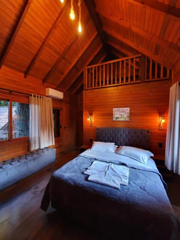 suíte da Pousada Árvore da Coruja em Gramado mostrando o lado interno de uma das cabanas com uma cama de casal e um pufe estofado cinza ao lado.