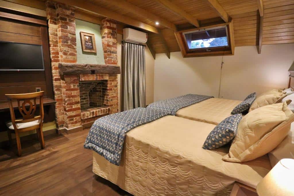 suíte da Pousada Serra Paradiso em Gramado com duas camas de solteiro unidas no lado direito do quarto, uma lareira em frente as camas e uma porta acortinada no canto.