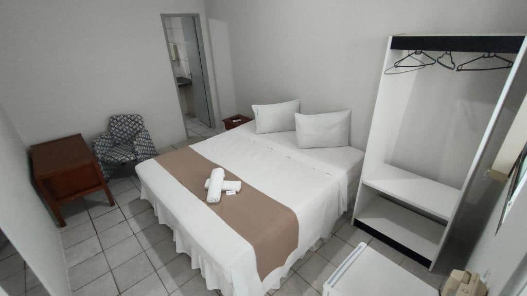 Uma poltrona com uma cômoda no canto esquerdo. Uma cama de casal no lado direito com um pequeno guarda-roupa. Um frigobar e a porta do banheiro. Foto para ilustrar post sobre hotéis perto do Consulado Americano em Recife.