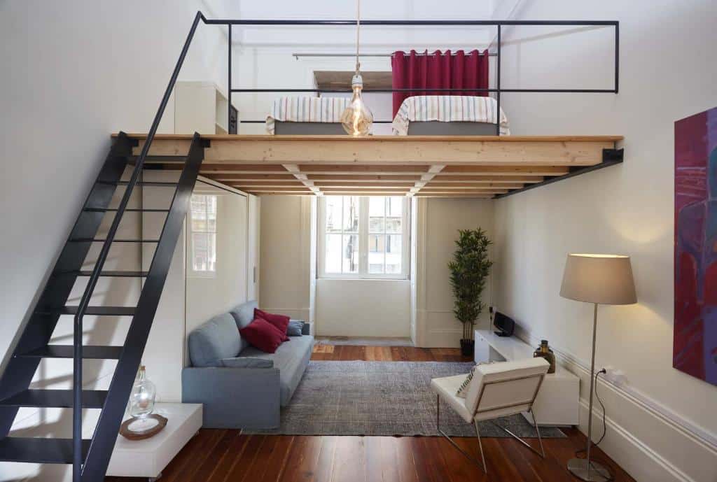 Quarto do The Passenger Hostel, a sala fica a frente com sofá e poltrona, do lado esquerdo tem uma escada que dá acesso a um cômodo que tem duas camas de solteiro. Representa Porto.