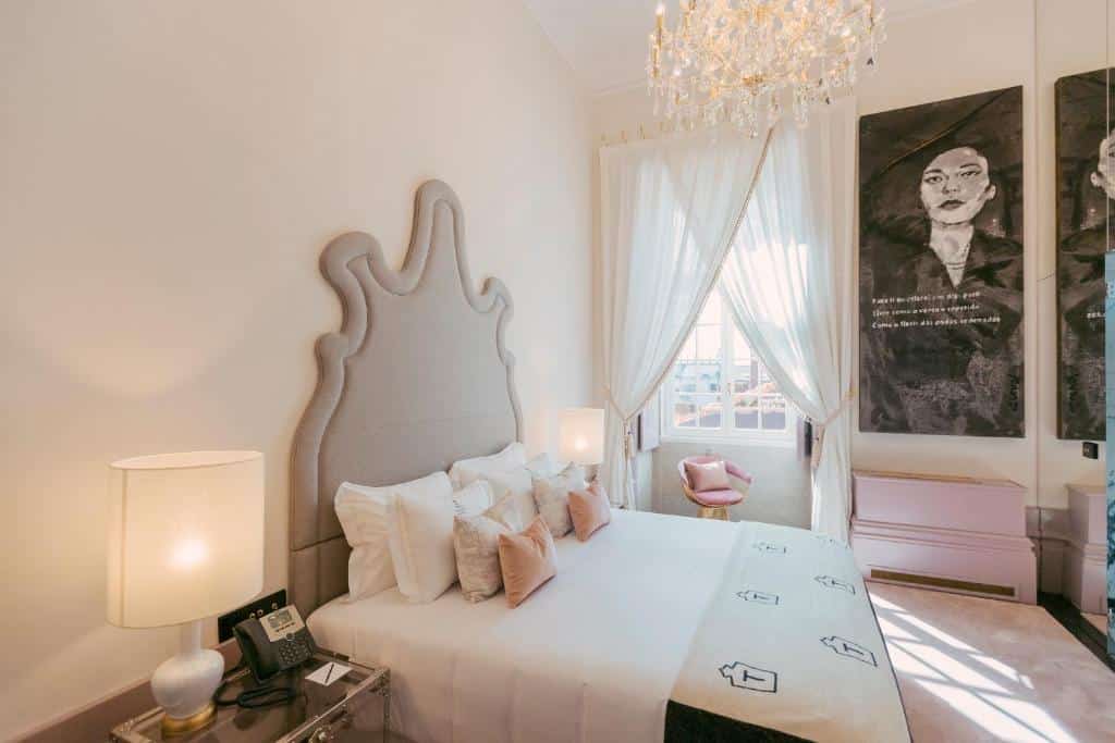 Quarto do Torel Palace Porto com cama de casal do lado esquerdo da imagem, com uma cômoda do lado direito da cama com luminária e telefone. Representa hotéis para lua de mel em Portugal.
