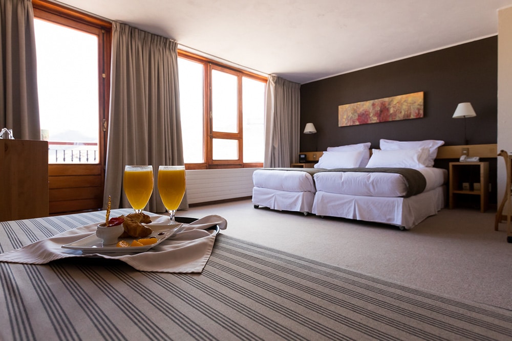 Quarto do Hotel Valle Nevado com dois sucos em cima de uma mesa a frente e ao fundo duas camas de solteiros juntos com duas cômodas do lado da cama.