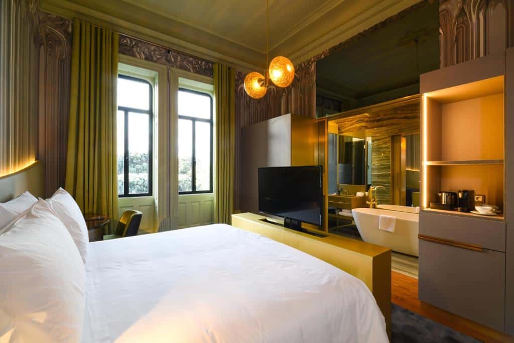 Quarto do Vila Foz Hotel & SPA – member of Design Hotels com cama de casal do lado esquerdo, uma TV em frente a cama e ao fundo banheiro privativo com banheira. Representa hotéis de luxo no Porto.