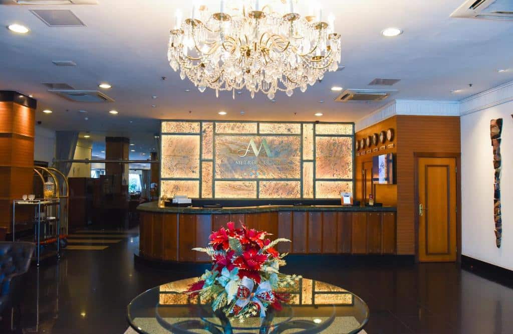 Recepção de hotel luxuoso com lustre grande e dourado no teto, decoração dourada no balcão ao fundo e mesa com flores ao centro. Imagem para ilustrar o post hotéis em Teresina.