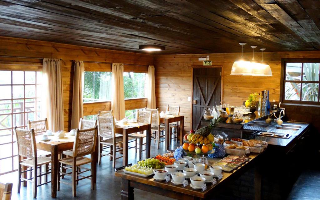 interior do refeitório dos chalés da montanha para representar onde ficar em Gramado. Há uma mesa à direita com vários pratos repletos de frutas, doces, geleias, pães e frios.