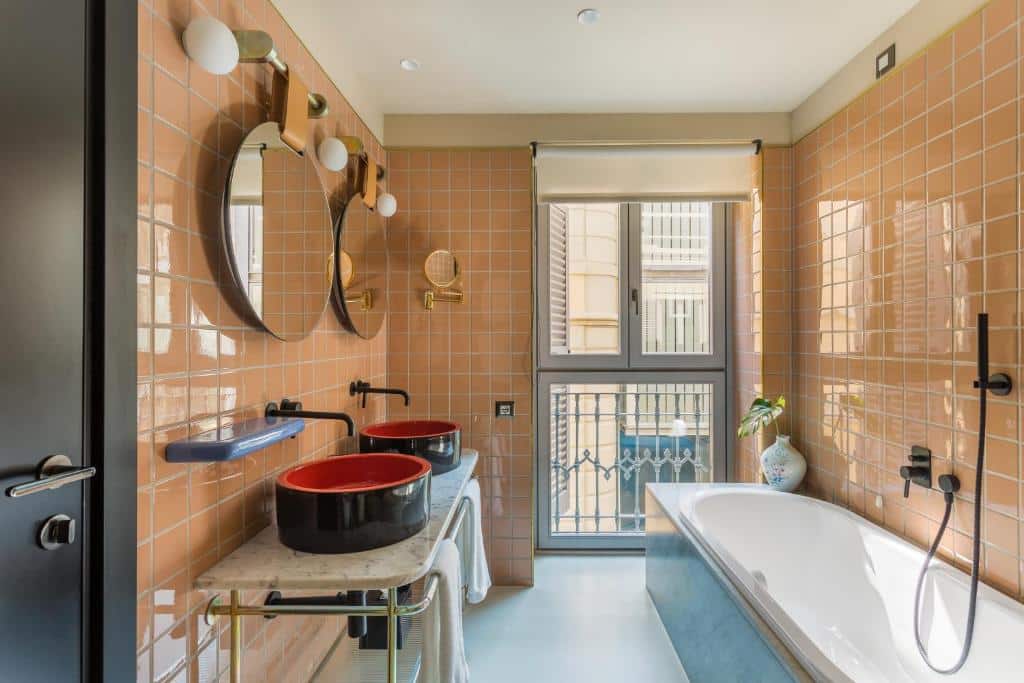 Banheiro do Room Mate Giulia com uma banheira de hidromassagem com uma janela, há um móvel com duas cubas redondas e dois espelhos redondos