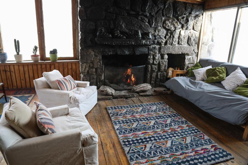 Sala de estar do Cordillera Hostel com duas poltronas brancas do lado esquerdo, uma lareira ao meio e do lado direito um sofá. Representa onde ficar no Valle Nevado.