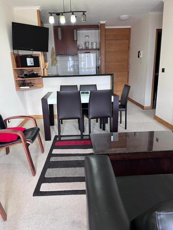 Sala dej antar Dúplex En com mesa com cinco cadeiras a frente e ao fundo uma TV e cozinha compacta.