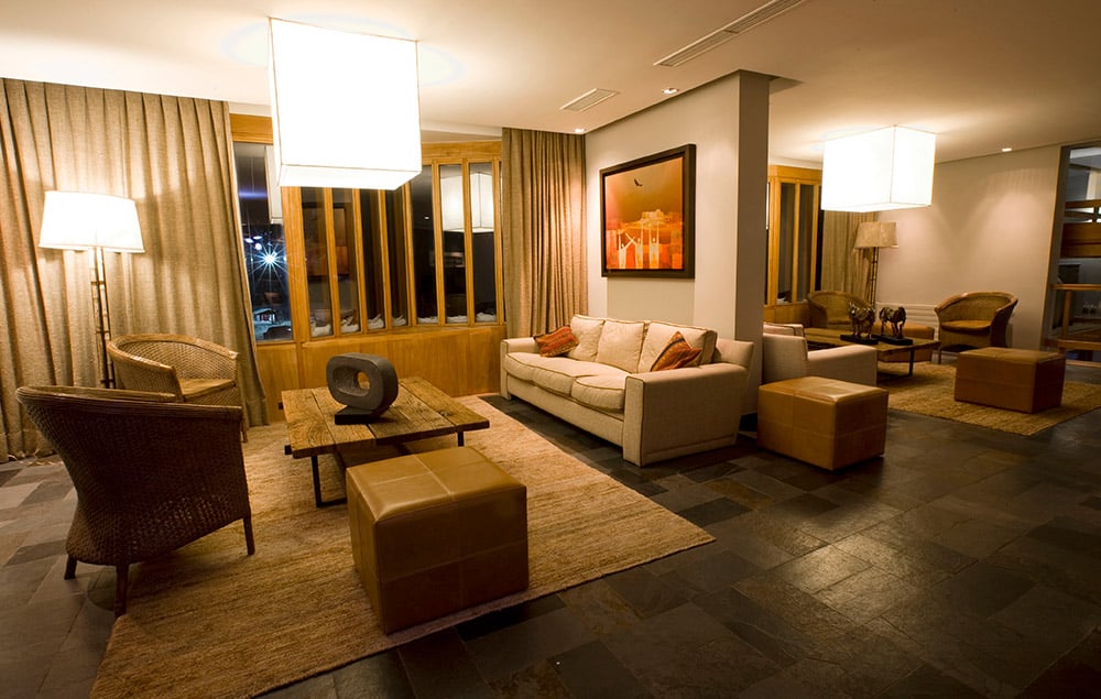 Sala do Hotel Puerta del Sol com sofás, poltronas e mesa ao centro.