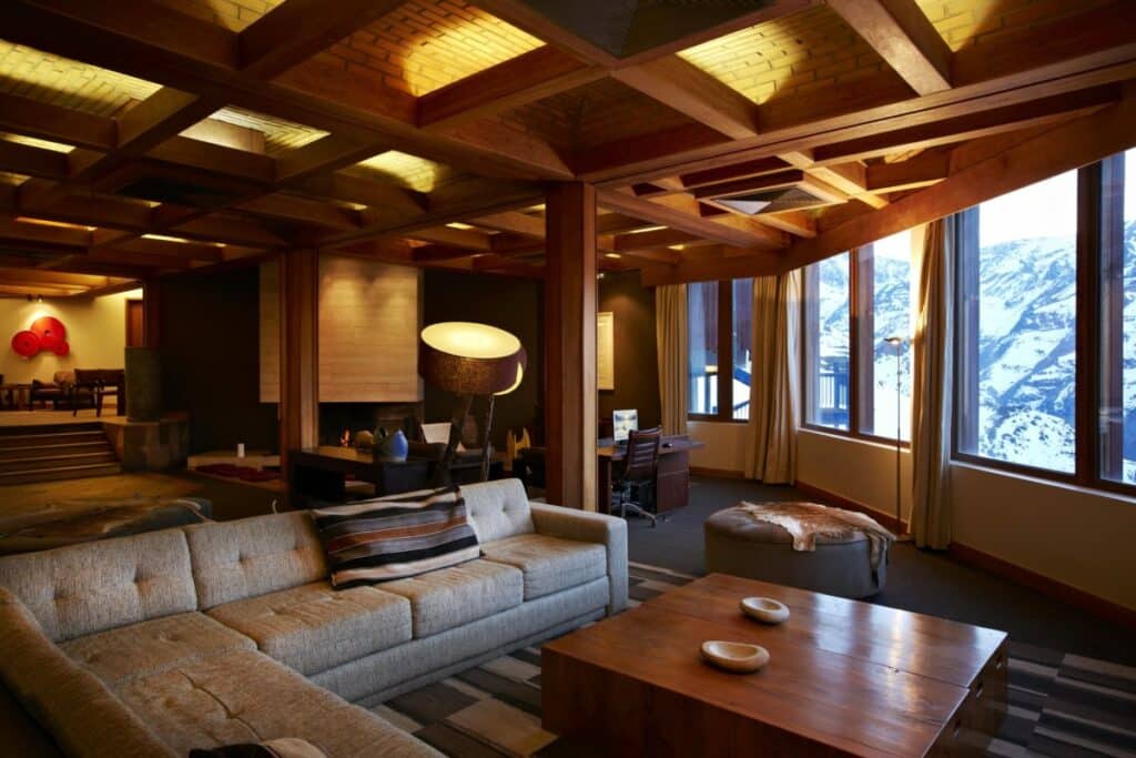 Sala de estar do Hotel Valle Nevado com sofá cinza do lado esquerdo uma mesa de madeira no centro da sala.