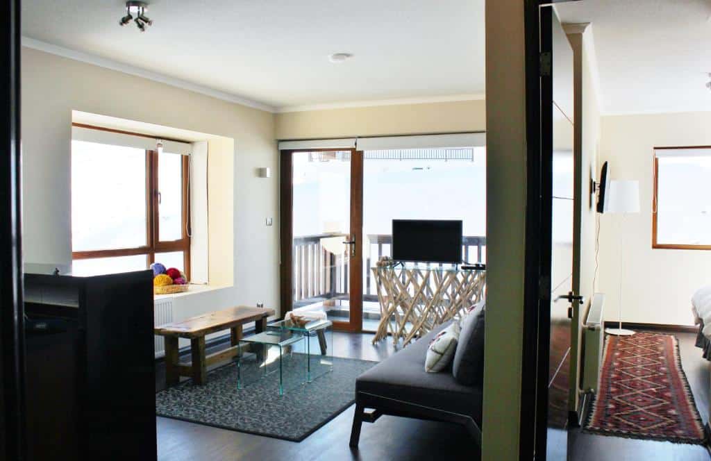 Sala do Vip Apartment Ski Out-In no lado esquerdo da imagem com sofá, mesa de centro e TV, do lado direito uma porta que dá acesso ao quarto.