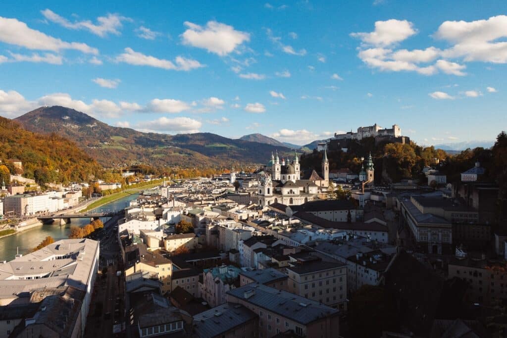 Imagem aérea da cidade de Salzburg com várias construções em modelo antigo, um rio ao lado e montanhas ao fundo durante o dia, ilustrando post hotéis em Salzburg.